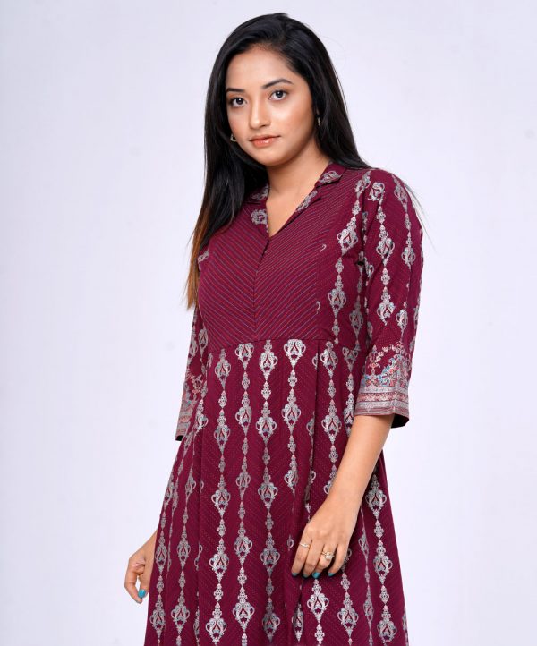 Burgundy all-over printed A-line Tunic in Viscose fabric. Features a lapel collar with hook closure at the front and three-quarter sleeves. Embellished with swing stitches and patch attachment at the top front. Pleats from the waistline.